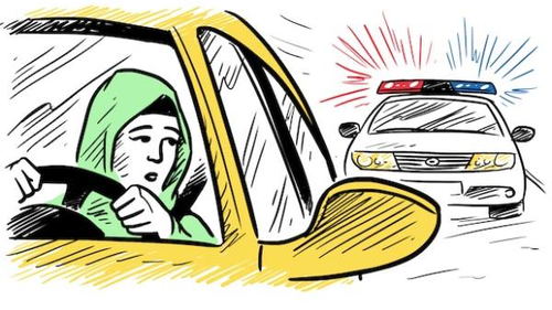 A woman wearing a green headscarf is driving a yellow car, looking worried as she glances in the rearview mirror. Behind her, a police car with flashing red and blue lights is approaching.