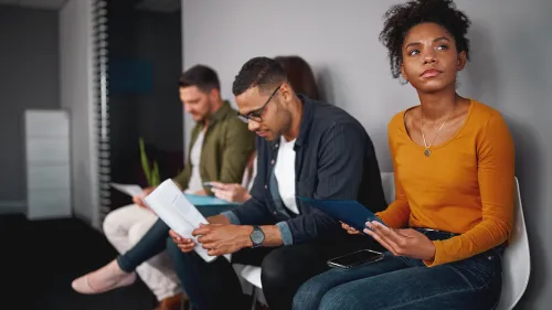 Photo of four people sitting in chairs waiting for a job interview.