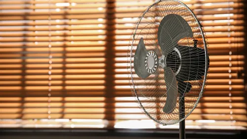 Photo of a fan near closed window shades that block the sunlight.