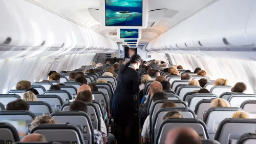 Interior of an airplane cabin with passengers seated in rows, a flight attendant in the aisle