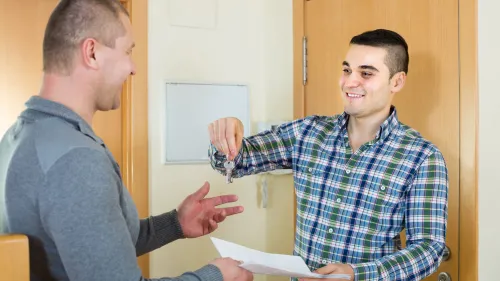 A smiling tenant receives the keys and lease agreement to his new apartment from a housing representative.
