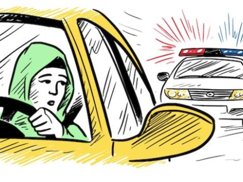 A woman wearing a green headscarf is driving a yellow car, looking worried as she glances in the rearview mirror. Behind her, a police car with flashing red and blue lights is approaching.