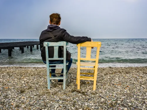 Fotografía de un hombre en una silla frente al mar al lado de una silla vacía.