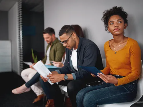 Photo of four people sitting in chairs waiting for a job interview.