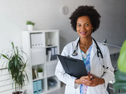 A female doctor with a stethoscope around her neck and holding a clipboard
