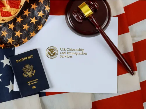 A U.S. passport, a judge's gavel, and an envelope from U.S. Citizenship and Immigration Services are laid on an American flag.