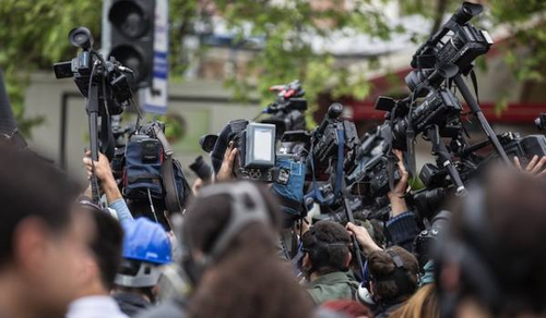 A large group of journalists and cameramen with video cameras and microphones gathered at an outdoor event. The scene is crowded, with cameras pointed in various directions, indicating a media frenzy.