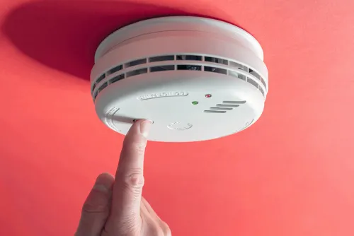 Photo of a person’s finger pressing a button on a smoke alarm to test it.