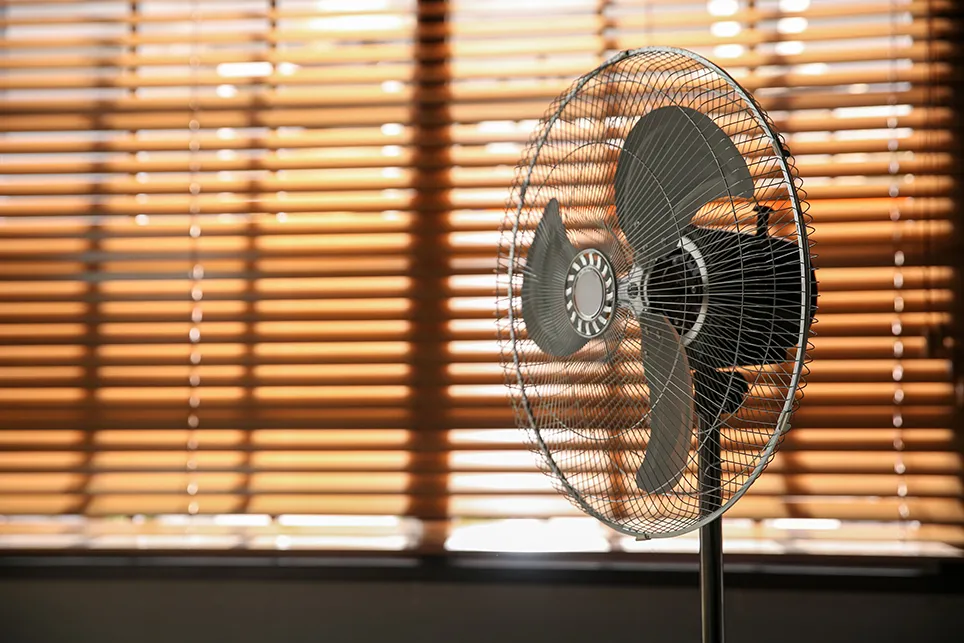 Photo of a fan near closed window shades that block the sunlight.