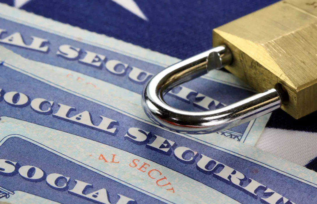 Three social security cards on a table with a padlock sitting just above them