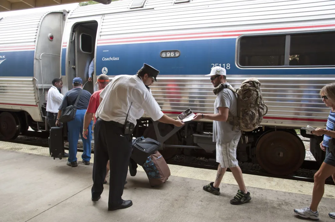 Passengers board a train. A conductor checks a passenger's ticket as he boards the train.